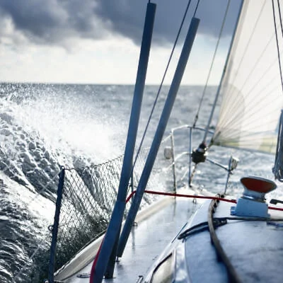 A close-up view from the deck of a sailing yacht cutting through ocean waves, showcasing the adventure and thrill of open sea sailing under dynamic weather conditions.