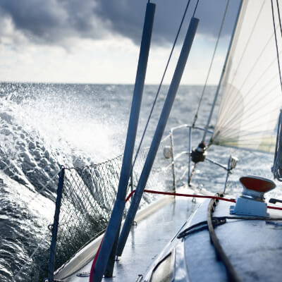 A close-up view from the deck of a sailing yacht cutting through ocean waves, showcasing the adventure and thrill of open sea sailing under dynamic weather conditions.