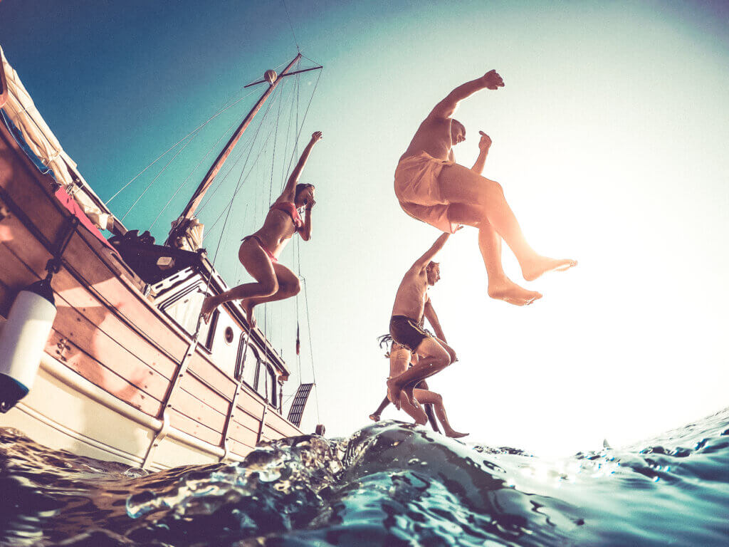 Group of friends jumping off a sailing boat into the sea, enjoying a summer adventure on the water